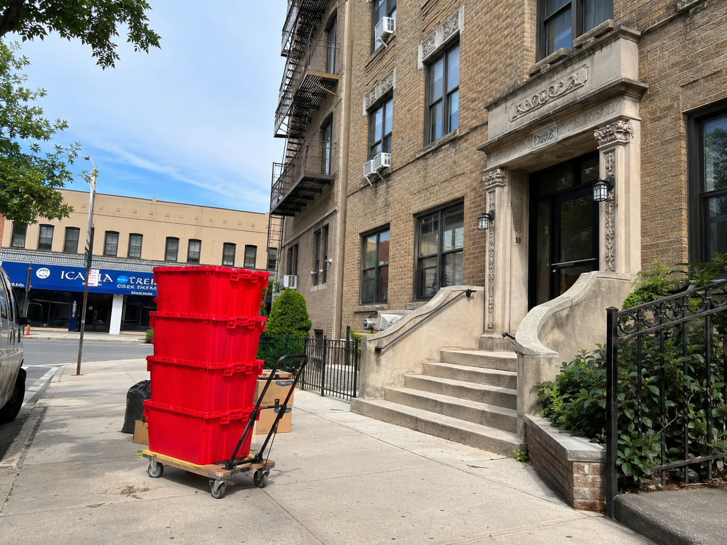EazyCrate moving bins on a dolly on an Astoria sidewalk with elevated N/W train tracks overhead — authentic Queens transit neighborhood moving context